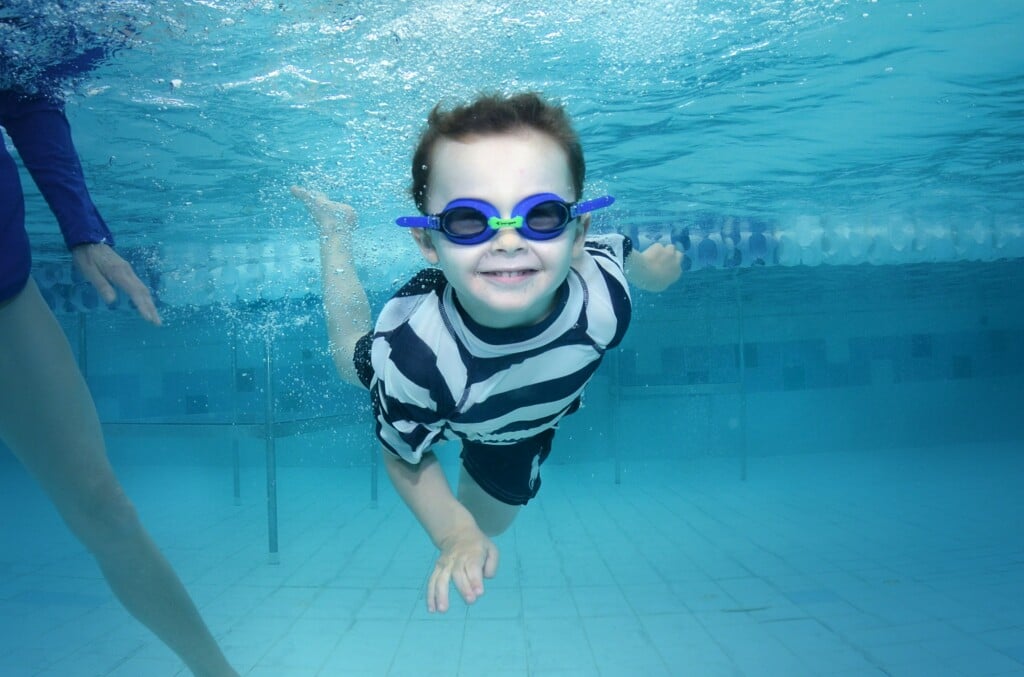 a smiling boy with goggles swimming underwater