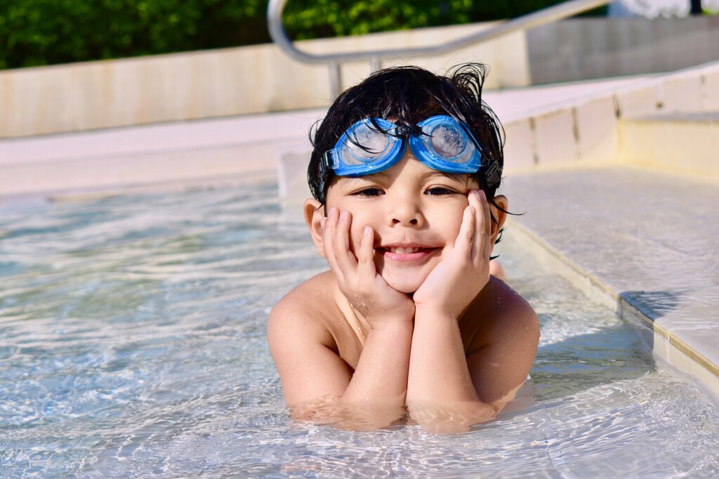 boy smiling while on the steps of a pool