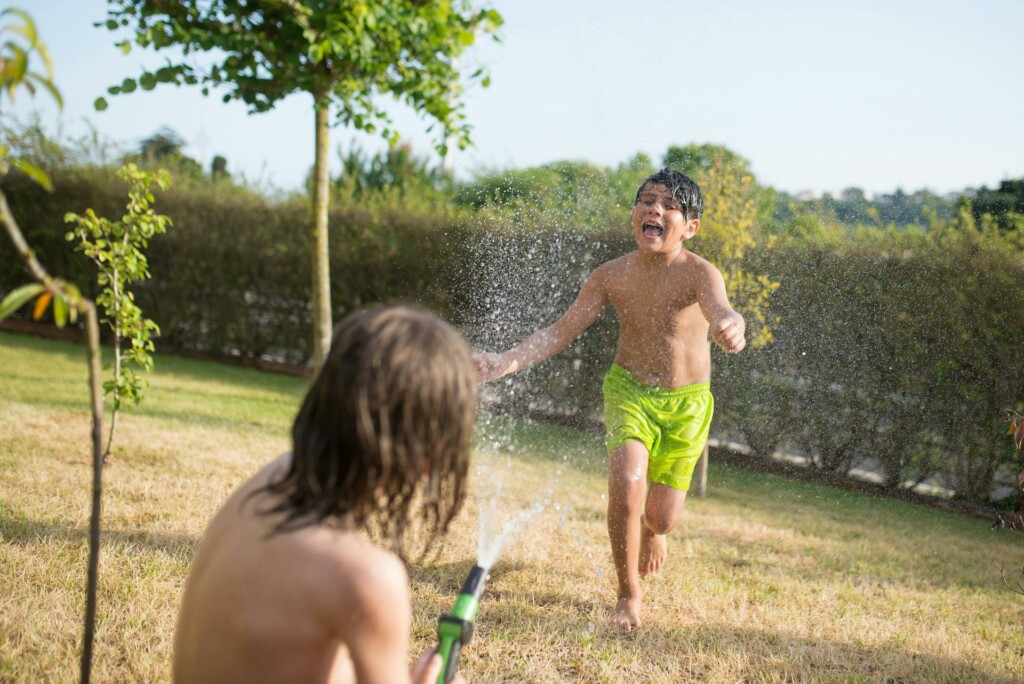 Two kids playing with a water hose in their backyard